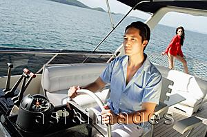Asia Images Group - Man at helm of yacht, woman in the background