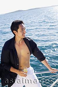 Asia Images Group - Man on boat, leaning on railing, drink in hand, looking away, smiling