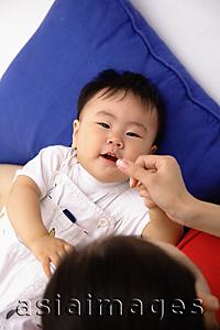 Asia Images Group - Baby boy lying on back, mother touching his lips