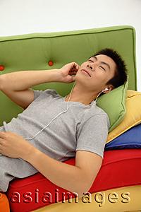 Asia Images Group - Man lying on sofa, listening to personal stereo