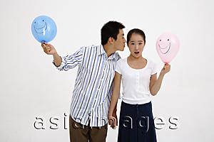 Asia Images Group - Couple holding balloons, man leaning over to kiss woman on cheek