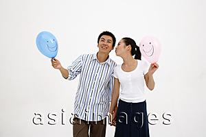 Asia Images Group - Couple holding hands, holding balloons, woman kissing man on cheek