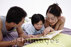 Asia Images Group - Family with one child lying on bed, reading book