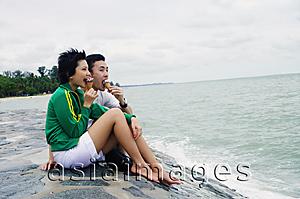 Asia Images Group - Couple sitting on breakwater, eating ice cream cones