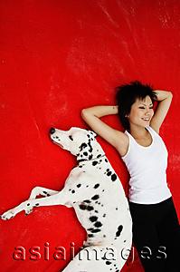 Asia Images Group - Woman with hands behind head lying down with Dalmatian on red blanket