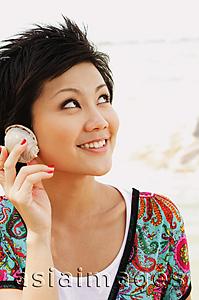 Asia Images Group - Woman holding shell to ear, looking away