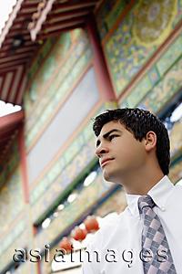 Asia Images Group - Businessman standing in front of temple gate, looking away, head shot