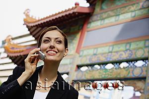 Asia Images Group - Businesswoman on mobile phone, standing in front of temple gate