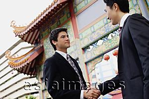 Asia Images Group - Two businessmen shaking hands, temple gate in the background