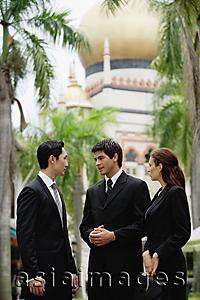 Asia Images Group - Two businessmen and one businesswoman standing, having a discussion, mosque in the background