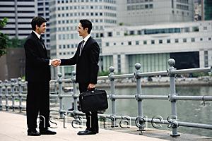 Asia Images Group - Two businessmen shaking hands, buildings in the background