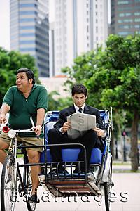 Asia Images Group - Businessman on trishaw, reading newspaper