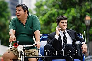 Asia Images Group - Businessman sitting in trishaw, using mobile phone