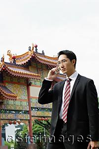 Asia Images Group - Businessman standing in front of Chinese temple, using mobile phone