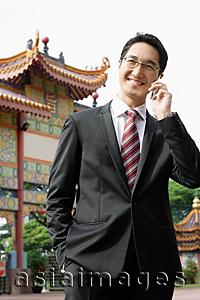 Asia Images Group - Businessman using mobile phone, standing in front of Chinese temple