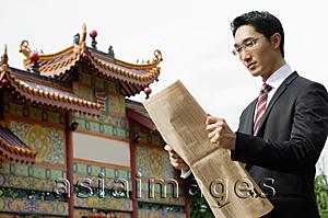 Asia Images Group - Businessman reading newspaper, Chinese temple in the background