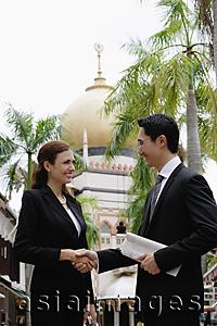 Asia Images Group - Businessman and businesswoman shaking hands, Mosque in the background