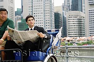 Asia Images Group - Businessman sitting in trishaw, holding newspaper