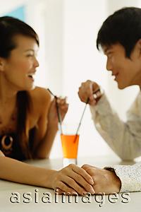 Asia Images Group - Couple sharing one drink, sitting face to face, holding hands