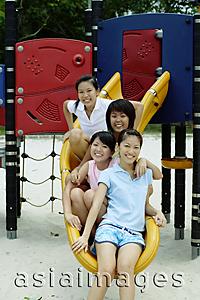 Asia Images Group - Young women sitting on slide, smiling at camera