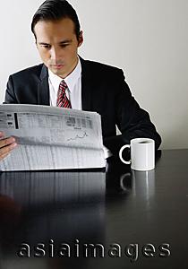 Asia Images Group - Businessman sitting at table reading newspaper, mug on table next to him