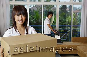 Asia Images Group - Woman carrying a box, smiling at camera, man in the background