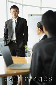 Asia Images Group - Businessman standing before seated colleagues, smiling at camera