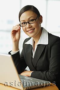 Asia Images Group - Businesswoman sitting in front of laptop, smiling at camera, portrait