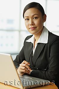 Asia Images Group - Businesswoman sitting in front of laptop, looking at camera, portrait