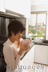 Asia Images Group - Young woman in kitchen, drinking from mug
