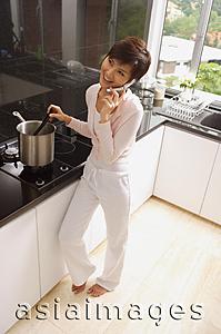 Asia Images Group - Young woman in kitchen, cooking and using mobile phone