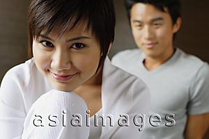 Asia Images Group - Woman resting chin on knee, smiling at camera, man in the background