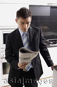Asia Images Group - Businessman in kitchen, looking at newspaper
