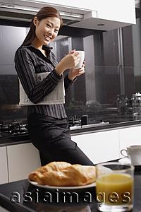 Asia Images Group - Female executive standing in kitchen, holding mug