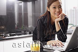 Asia Images Group - Female executive in kitchen with laptop, hand on chin, smiling at camera