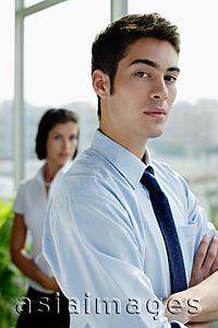 Asia Images Group - Male executive with arms crossed, looking at camera, woman in the background
