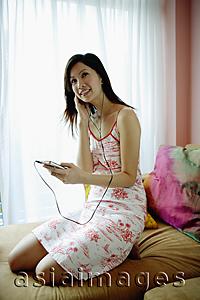 Asia Images Group - Woman on bed, listening to MP3 player