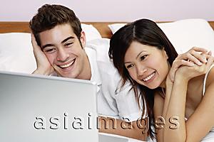 Asia Images Group - Couple lying on bed, looking at laptop