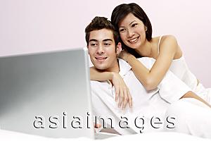 Asia Images Group - Couple on bed, looking at laptop, woman embracing man