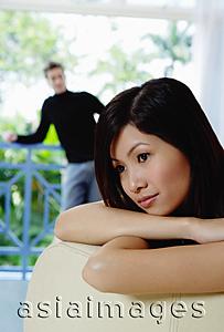 Asia Images Group - Woman leaning on back of sofa, looking away, man in the background