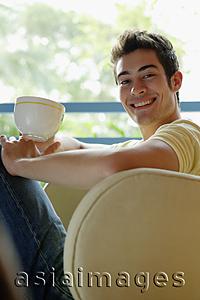 Asia Images Group - Man sitting on armchair, holding cup, smiling at camera