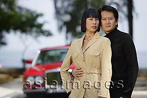 Asia Images Group - Couple standing side by side, looking at camera, car in the background