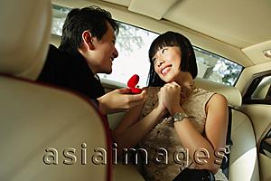 Asia Images Group - Couple sitting in backseat of car, man holding ring box, woman smiling with hands clasped