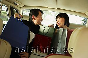 Asia Images Group - Couple sitting in backseat of car, looking at each other, shopping bags on their laps