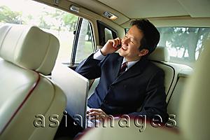 Asia Images Group - Businessman in backseat of car, using laptop and mobile phone