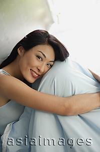 Asia Images Group - Woman sitting on bed, hugging knees, smiling at camera