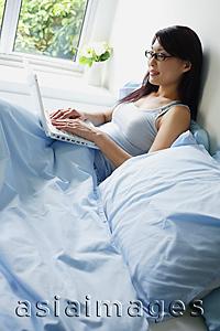 Asia Images Group - Woman using laptop in bedroom