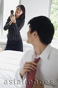 Asia Images Group - Man adjusting tie, turning to look at woman behind him