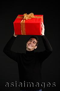 Asia Images Group - Man in black turtleneck, holding wrapped present over his head