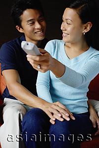 Asia Images Group - Couple sitting side by side, woman holding TV remote control